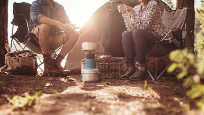 Two campers sitting in chairs outside with a camp stove between them, tent in the background